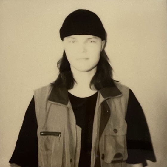 Sepia portrait of Mikass in a beanie and vest.